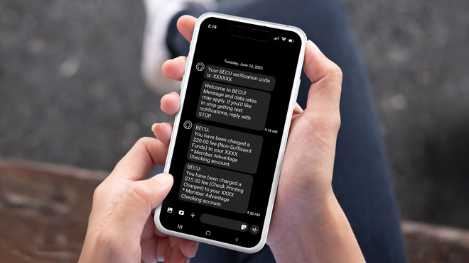 A close-up of a person's hands holding a smartphone displaying text messages about fee charges. Their lap is visible, suggesting they are seated and reading the alerts.