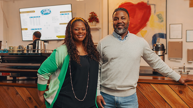 BECU member Michelle L. and her husband standing in front of a coffee shop counter, with a menu and coffee supplies visible in the background.