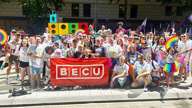 BECU employees, friends and families gather for a photo behind a red BECU banner during the Seattle Pride Parade.