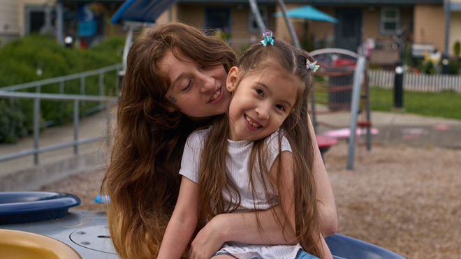 A mother hugs her smiling daughter at a playground.