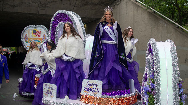Spokane Lilac Festival royalty ride on a decorated parade float in coordinated purple dresses.