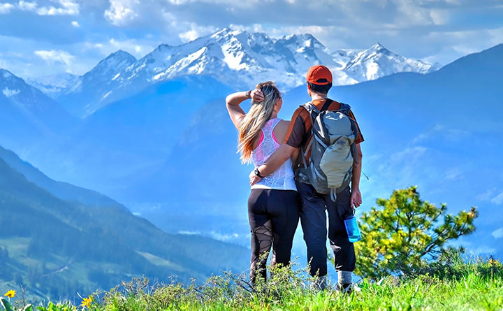 A couple stands at a viewpoint looking out over a valley with the North Cascades in the background.