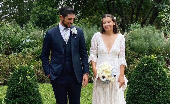 Groom in dark suit and bride in wedding gown stand smiling in garden