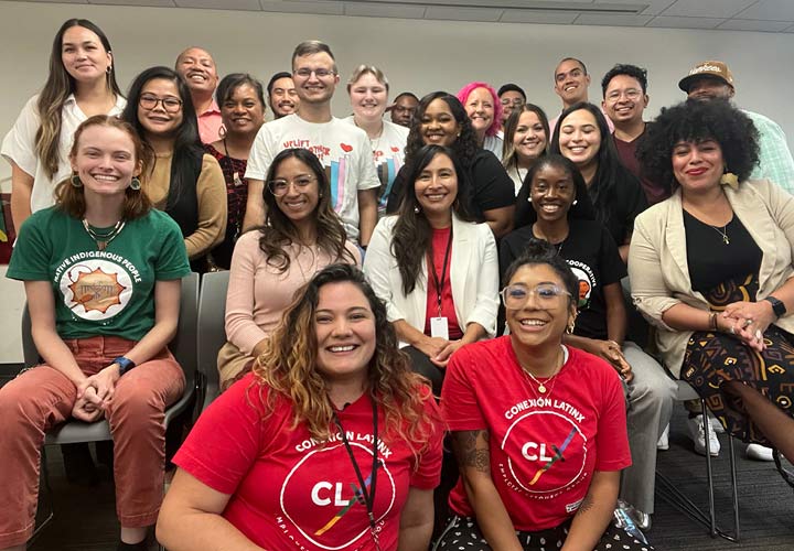 A group of BECU's Latinx Employee Resource Group (ERG) are gathered together for a photo inside. Two members are kneeling at the front of the group photo, while others sitting in chairs and standing. 