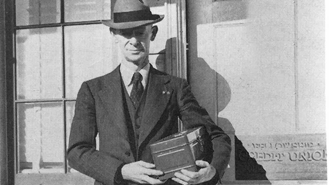man in a suit and hat holding a metal box, founding member, Elmer