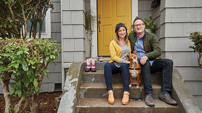 A man and a woman sitting on their front door steps with a dog