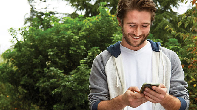 A smiling man outdoors looking at a mobile phone
