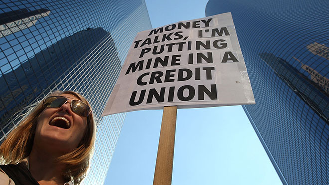 A woman holding a sign that says, "Money Talks, I'm putting mine in a credit union".