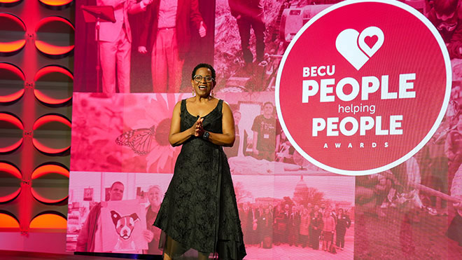 a woman standing on a stage with the People Helping People banner behind her