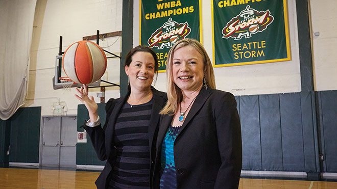 two woman standing on a basketball court, one holding a basketball